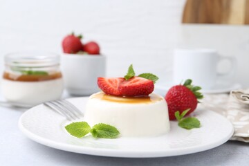 Tasty panna cotta with caramel, strawberries and mint on light table, closeup