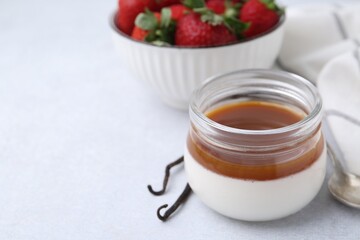 Tasty panna cotta with caramel, vanilla pods and strawberries on light table, closeup. Space for...