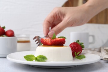 Woman eating tasty panna cotta at light table, closeup