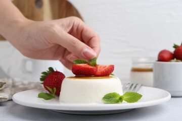 Woman decorating tasty panna cotta with mint at light table, closeup
