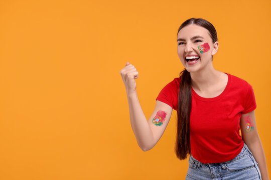 Excited fan with flags of Portugal painted on her body against orange background. Space for text