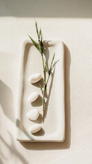 Smooth white stones and bamboo sprig resting on ceramic tray, illuminated by soft sunlight. Zen-inspired minimalist composition evoking calm and balance