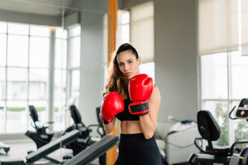 Fototapeta premium A woman wearing a red boxing glove. She is standing in front of a mirror. There are two exercise bikes in the background