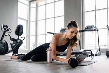 A woman is laying on the floor with a laptop and a water bottle. She is smiling. The laptop is open...
