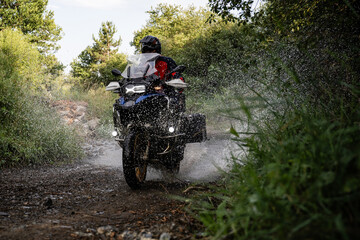 Motorcyclist riding through water on dirt road in forest