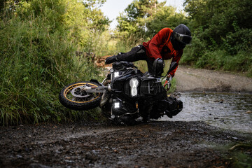 Motorcyclist lifting fallen adventure motorcycle on muddy trail
