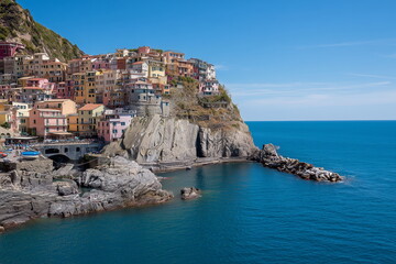 A breathtaking coastal town perched on a rugged cliffside, with colorful houses stacked closely together, overlooking the deep blue ocean under a clear sky--reminiscent of Cinque Terre, Italy.
