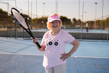 Senior woman holding racket is playing tennis on outdoor court