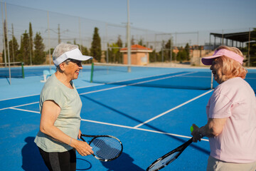 Two senior women playing tennis and smiling on a sunny day