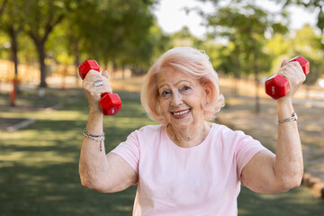 Senior woman lifting weights and smiling in park