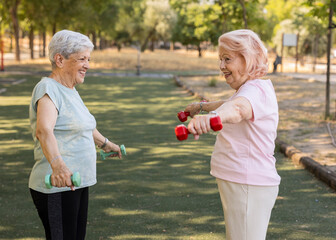 Senior women lifting weights and smiling in park, active seniors enjoying fitness