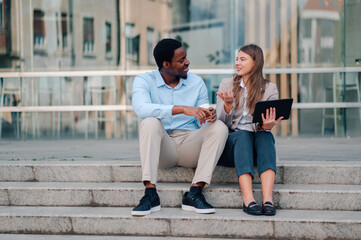 Business partners using tablet and talking about project sitting on stairs