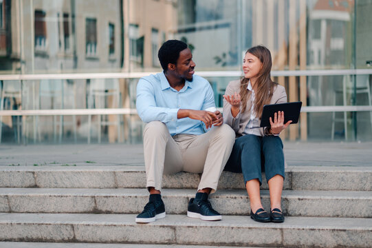 Business partners using tablet and talking about project sitting on stairs