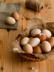 Rustic basket of farm fresh eggs on natural wooden table with linen and jute texture. Still life...