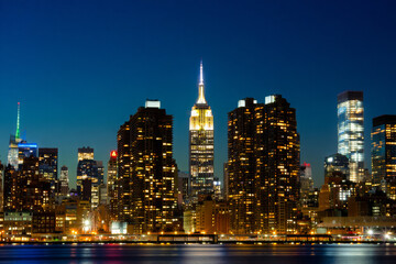 Naklejka premium Vibrant New York City skyline at night with reflections on the water, showcasing urban architecture and towering skyscrapers