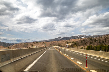 Local road with surrounding leafless trees mountains under cloudy sky in late winter season