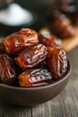 Vertical macro composition of glossy dried dates in a ceramic bowl placed on a natural wooden table surface in soft daylight tones