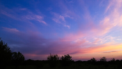 Twilight sky with crescent moon and dreamy pink-purple clouds above a dark rural landscape. Ideal for nature, backgrounds, or sunset-themed designs.