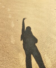 shadow cast on the sand of a young girl dancing with her arms in the air, backlit by the sun