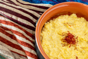 yellow Saffron rice with red threads garnish, rustic ceramic bowl, Risotto Milanese, traditional Italian, indian or oriental cuisine in brown bowl on brown and blue striped oriental fabric, high angle