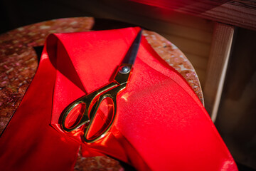 Golden scissors lie on a shiny red satin ribbon, set on a textured surface, suggesting preparation...