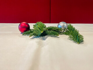 Merry Christmas decoration on dining table. Pine needle branches with red and silver ball on festive white tablecloth, red textile seat background, high angle view, copy space