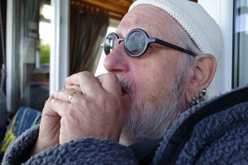 Senior man with beanie, glasses and a beard plays harmonica. He has individuality