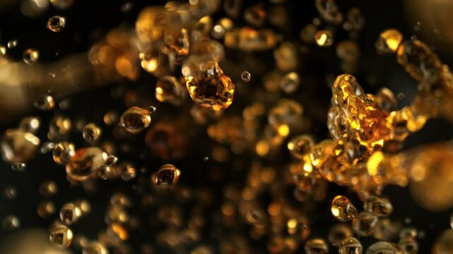 Super Slow Motion Shot of Flying Golden Liquid Drops Towards Camera on Black Background at 1000fps.