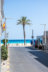 street with lights and palm tree in Cala Millor with sea in background - vertical
