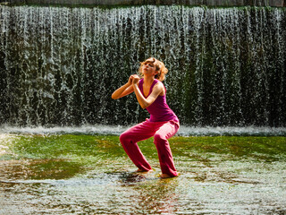 Young fitness girl model is standing in river water with stunning waterfall background. Girl is...