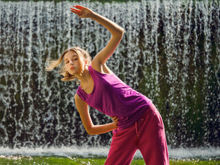 Young fitness girl model is standing in river water with stunning waterfall background. Girl is...