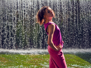 Young fitness girl model is standing in river water with stunning waterfall background. Girl is...