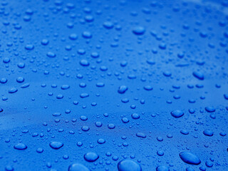 The image is of a blue surface with many small drops of water on it. The drops are scattered all...