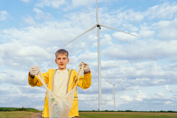 Teenage boy holding eco bag with collected bottles in front of wind turbine