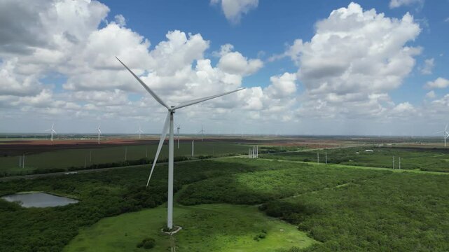 Wind turbine generates clean renewable electric energy in a green Texas field with a blue sky and white clouds. Aerial drone.