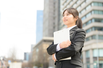 バインダーを持って微笑むリクルートスーツの日本人女性