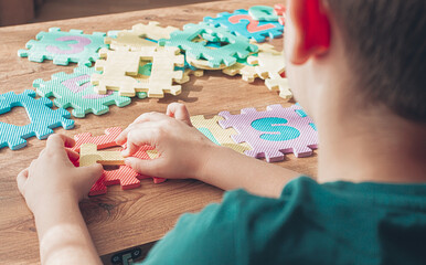 Child assembling colorful puzzle pieces on a wooden table in a bright indoor space during the day