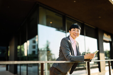 Portrait of a young asian japanese businesswoman woman using a smartphone mobile phone walking down...