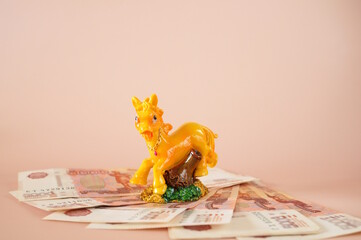 A horse figurine with paper bills on a pink background.