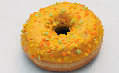 A vibrant yellow donut covered in colorful sprinkles rests on a plain light surface showcasing its...