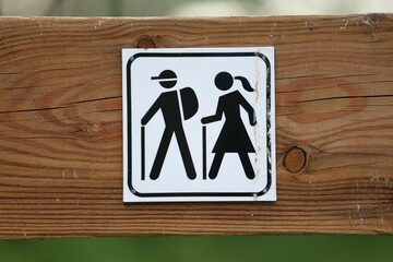 Close-up of a black and white hiking trail sign mounted on a wooden post. It shows male and female...