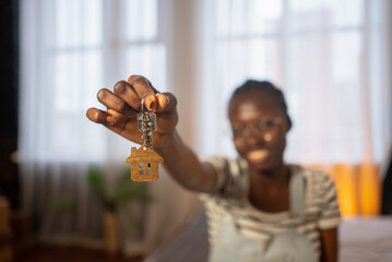 Excited young african american woman showing new house keys with house shaped keychain after buying her first apartment, celebrating real estate investment and property ownership