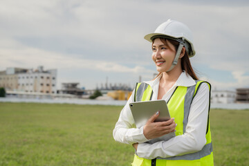 Female Engineer with Tablet Surveying Construction Site. A woman wearing a yellow vest and a hard...
