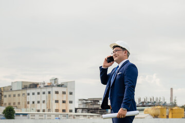Businessman or Investor Making a Phone Call at an Industrial Development Site. A man in a blue suit is talking on a cell phone