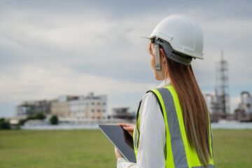 Female Engineer with Tablet Surveying Construction Site. A woman wearing a safety vest and a hard...