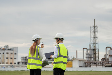 Title: Engineers Coordinating with Walkie-Talkie at an Industrial Plant. Two people wearing safety...