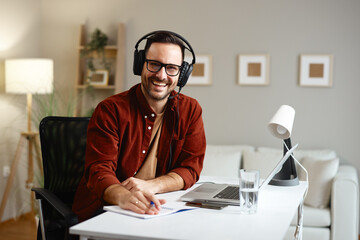 Smiling teacher wearing headset teaching online lesson and writing notes