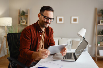 Smiling freelancer working from home using laptop and tablet