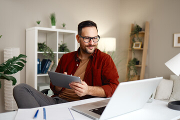 Freelancer working from home using laptop and tablet smiling