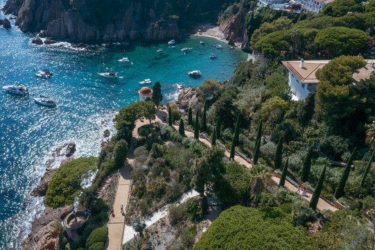 An aerial view showcases the stunning Marimurtra Botanical Garden, with its diverse flora, charming gazebo, and elegant villa overlooking the clear blue Mediterranean Sea.
